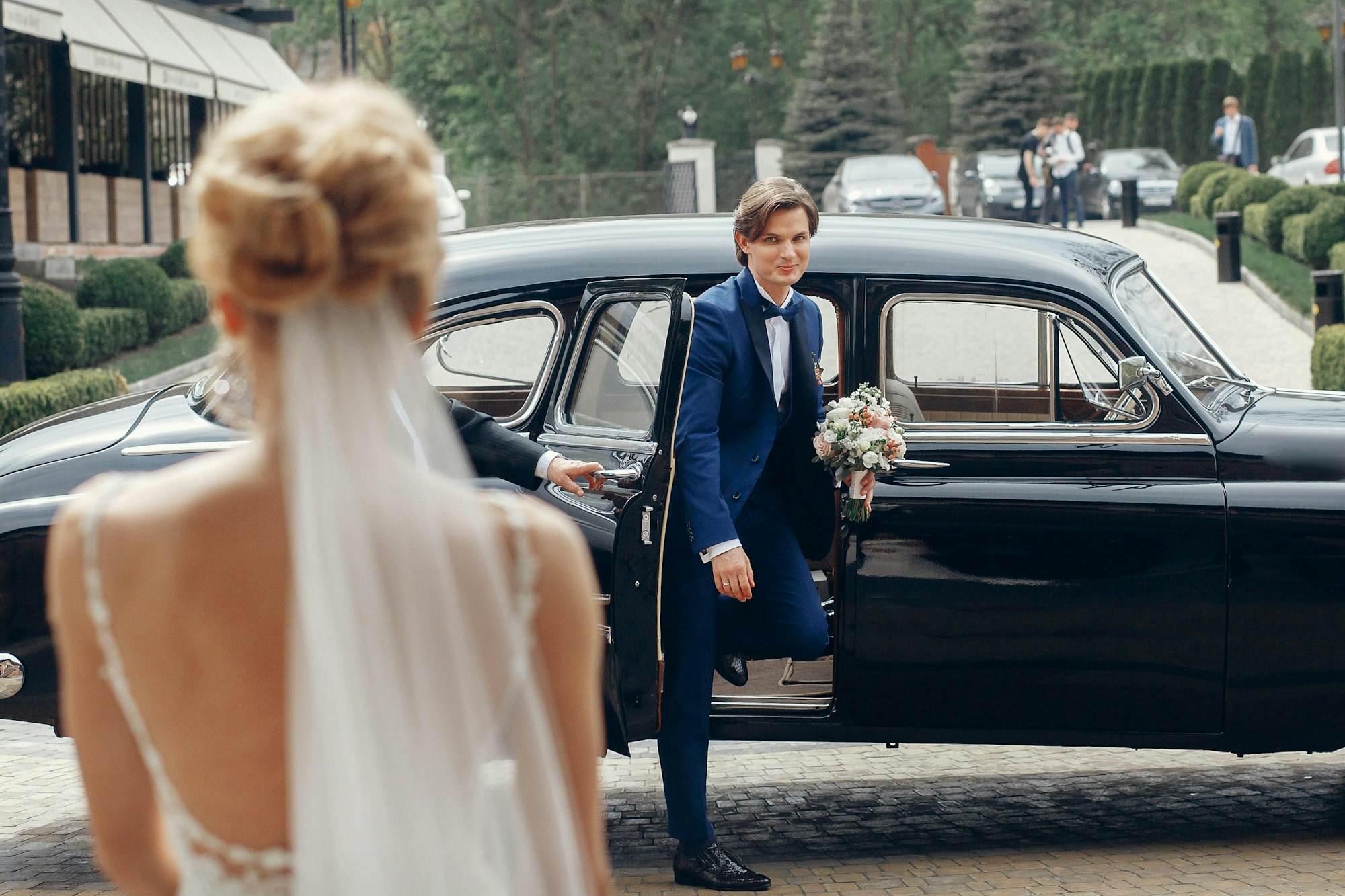 Bräutigam steigt mit Brautstrauß aus Hochzeitsauto und läuft auf seine Braut zu, damit sie zur freien Trauung gehen können.