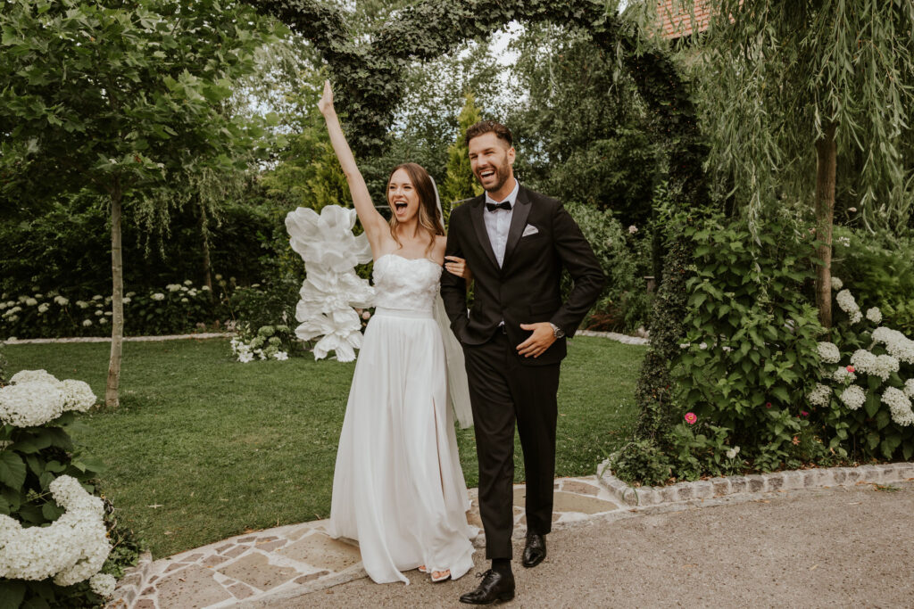 Braut wirft Hände hoch und jubelt für freie Trauung aud ihrer Hochzeit im Ausland. Der Bräutigam lacht