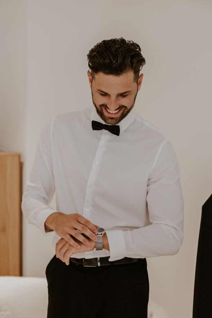 Bräutigam im Anzug mit Fliege sieht auf seine Uhr kurz vor der freien Trauung mit evylinandwords