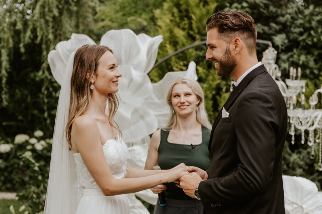 Traurednerin Evylin steht zwischen dem Brautpaar und hält die Traurede bei einer Hochzeit in Bayern. Sie sieht den Bräutigam an. Die freie Trauung ist auf deutsch und Englisch