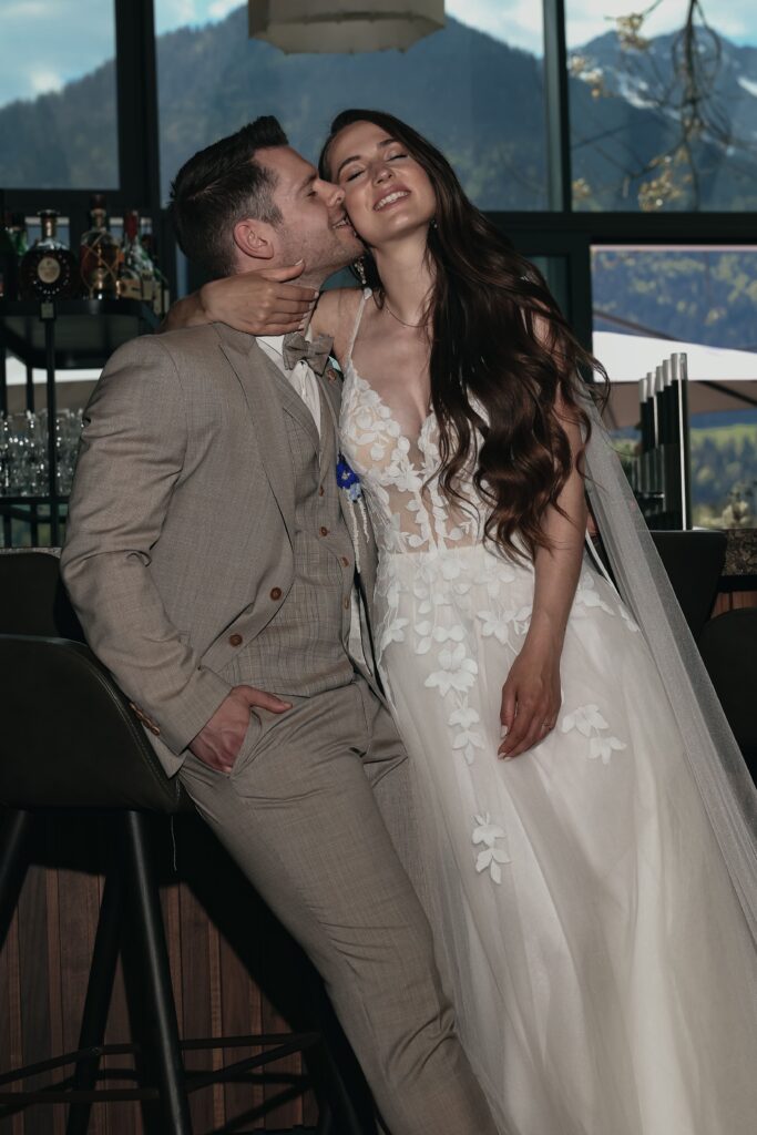 Elopement Wedding mit Brautpaar an einer Bar, der Bräutigam küsst seine Braut auf die Wange, bald beginnt die Trauung mit Trauredner Evylin aus Regensburg für Ingolstadt und Bayern