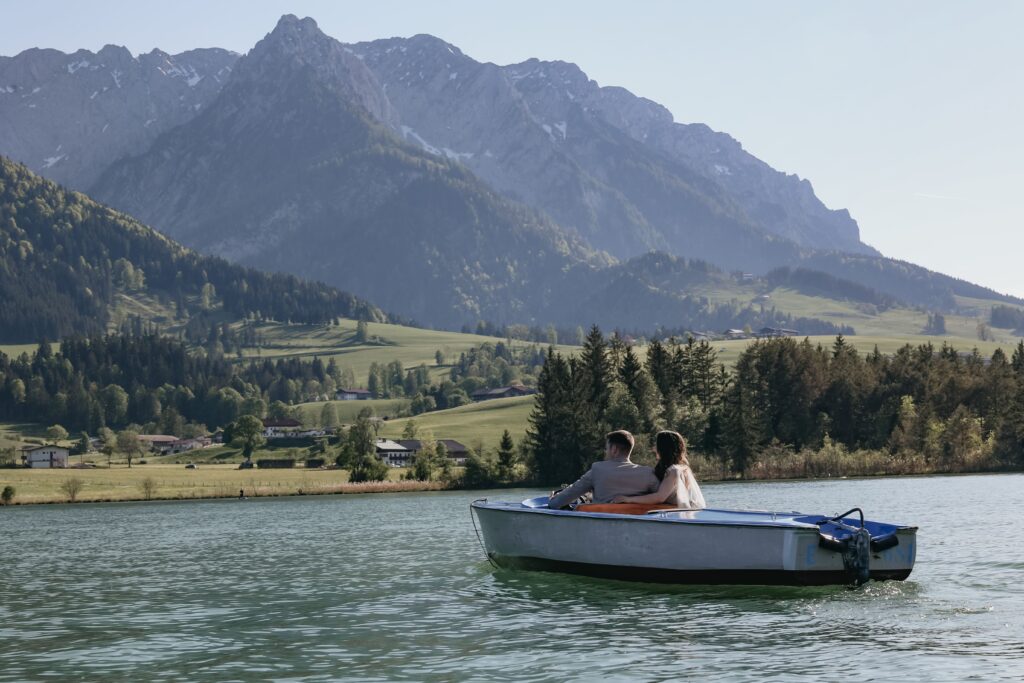 Hochzeit, das heiratende Paar fährt in einem Kahn im Wasser und im Hintergrund sind die Berge