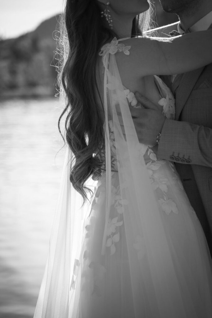 schwarz-weiß Nahaufnahme von Frau in weißem Kleid auf ihrer destination wedding, die ihren Ehemann umarmt