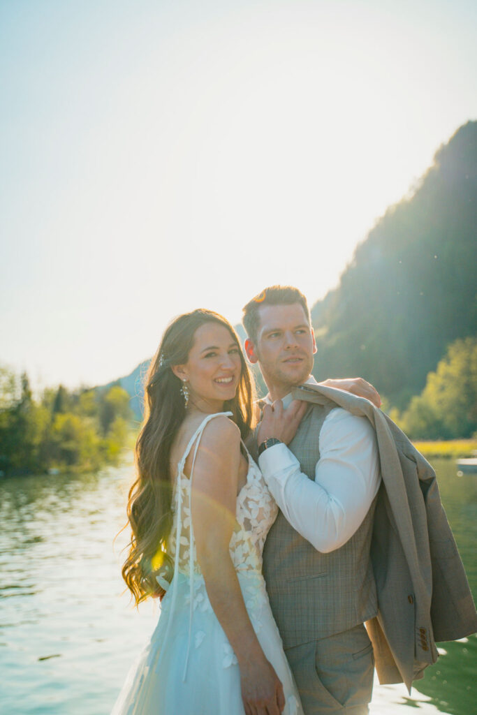 Bräutigam hat sein Jackett über seine Schulter geworfen und steht mit Braut an der Donau bei seiner destination wedding