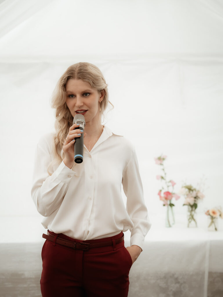 Trauredner für Hochzeiten Evylin aus Regensburg mit Mikrofon in der Hand erklärt den Hochzeitsgästen einige Punkte