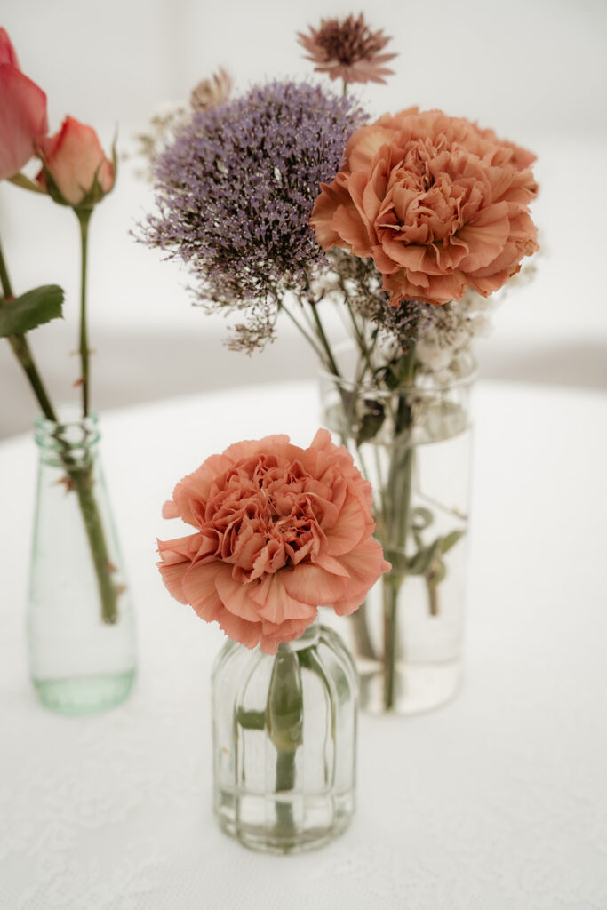 für eine Hochzeit stehen mehrere Vasen mit roten und violetten Blumen bereit